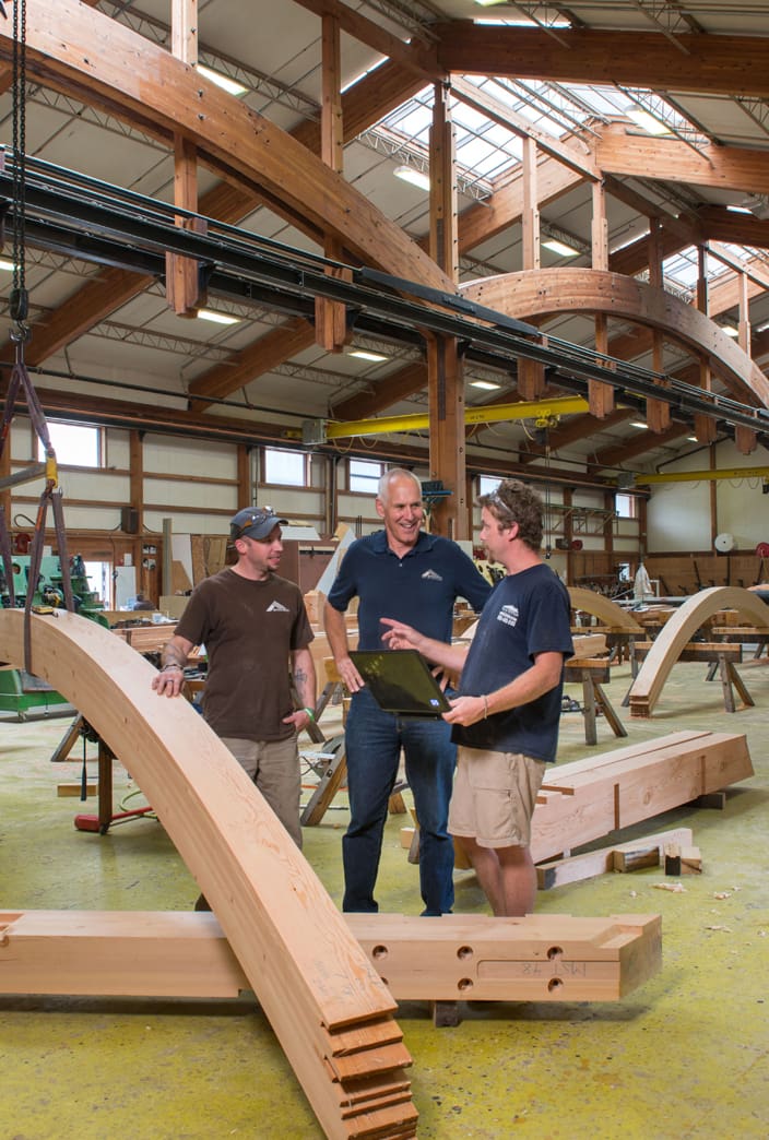 Tedd Benson talks with two employees about a complex timber structure
