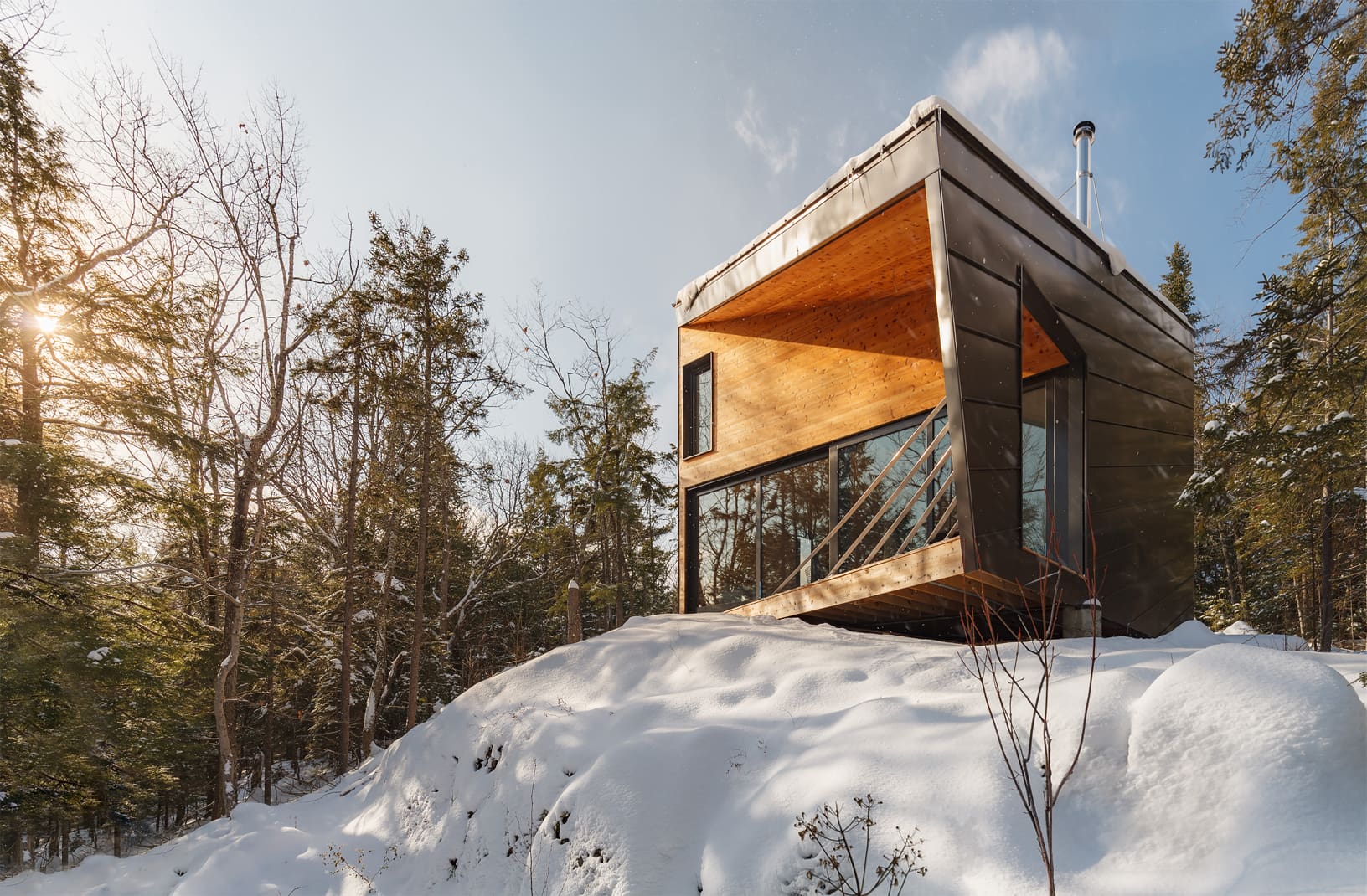 Side view of an angular modern prefab tiny house on a snowy hill