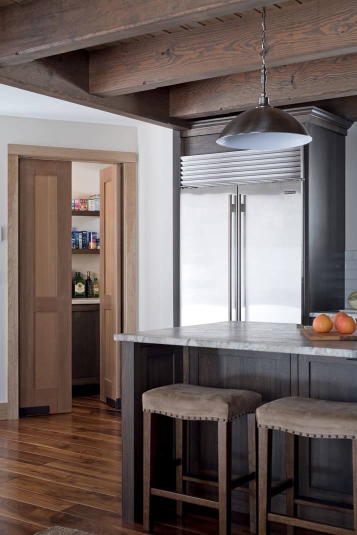 A stainless steel refrigerator sits next to a pantry with the door cracked open
