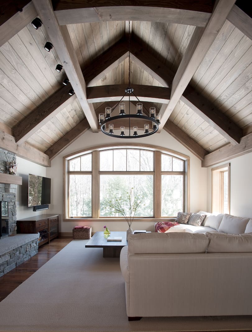 A vaulted timber ceiling, chandelier, and large window frame the living room in this energy efficient home